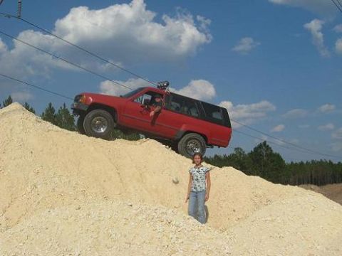1987 Toyota 4Runner - Red 1987 Toyota 4Runner tackles a steep dirt incline under a cloudy sky.