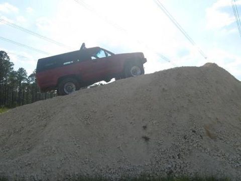 1987 Toyota 4Runner - A red SUV is shown driving up a large pile of dirt under a cloudy sky.