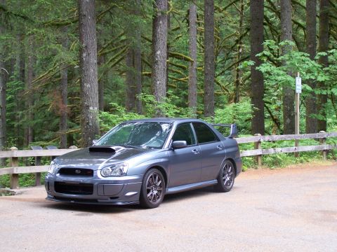 1998 Subaru Legacy - A gray Subaru Impreza WRX STI is parked in a wooded area next to a wooden fence.