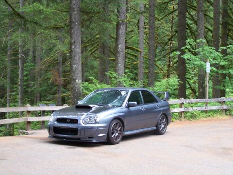 1998 Subaru Legacy - A gray Subaru Impreza WRX STI is parked in a wooded area with a wooden fence in the background.