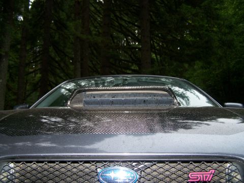 1998 Subaru Legacy - Close-up of a Subaru's front grille and hood scoop, a carbon fiber wrap and a pink STI badge.