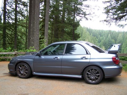 1998 Subaru Legacy - A gray Subaru Impreza WRX STI sedan is viewed from the side, parked in a wooded area.