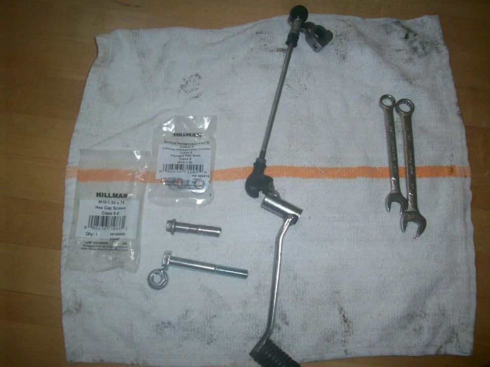 Motorcycle lever, linkage, bolts, wrenches, and Hillman M10 hardware packets on a white shop towel