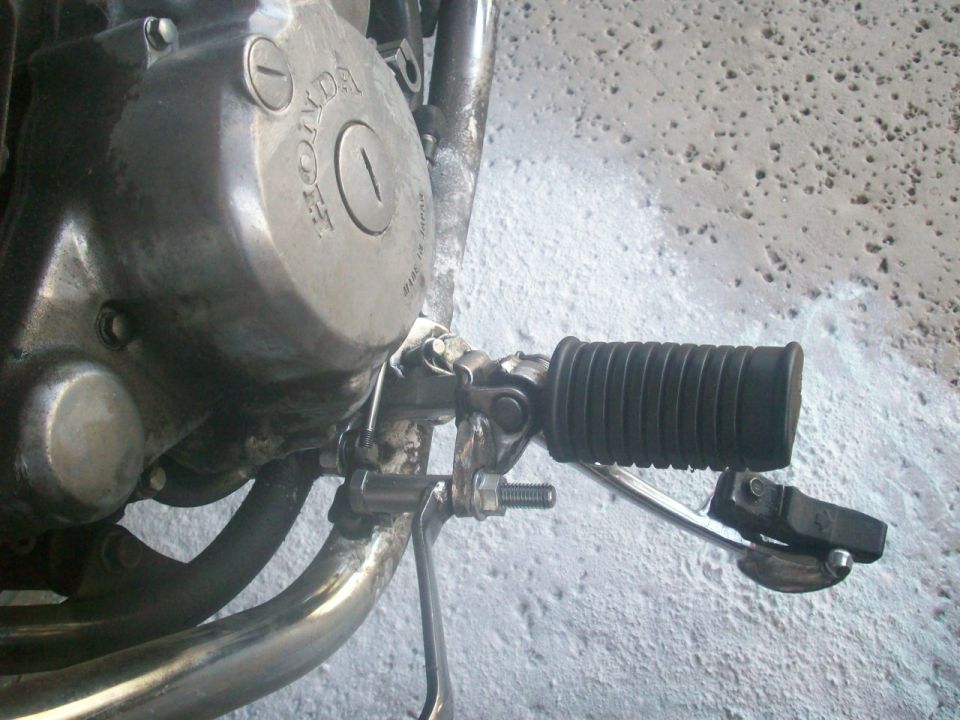 Close-up of Honda motorcycle engine cover, black rubber footpeg, kickstarter and brake pedal.