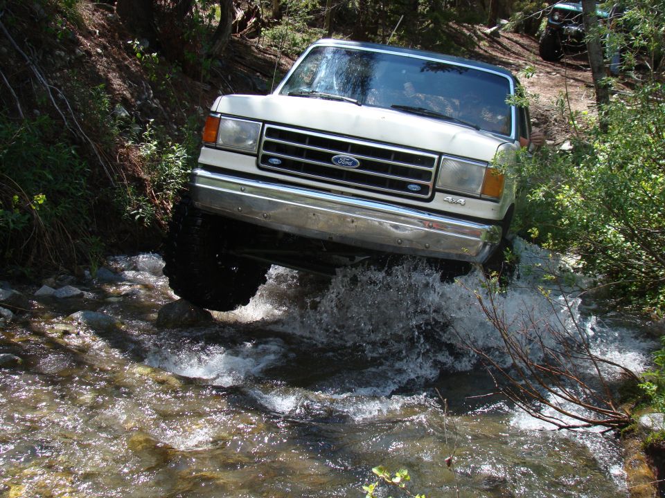 White Ford Bronco driving through a stream, front 3/4 view