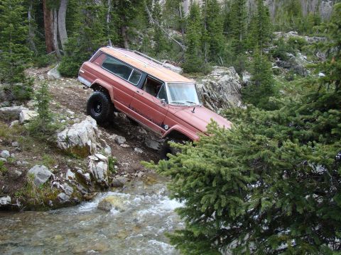 1989 Ford Bronco - A red Jeep Cherokee Chief navigates a challenging rocky stream bed during an off-road excursion.