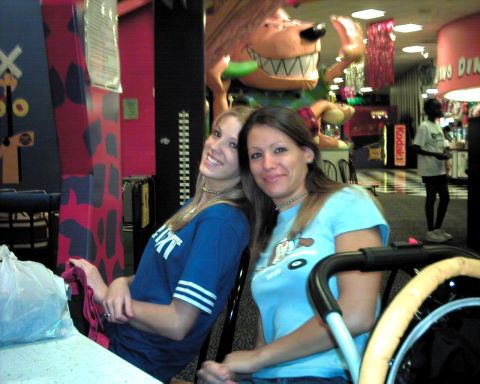 1990 Ford Taurus - Two women are seated in a brightly lit entertainment venue with colorful decorations and arcade games visible.