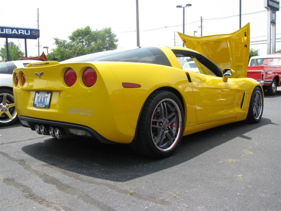 Yellow Chevrolet Corvette with hood open, parked next to a white car and a red pickup truck