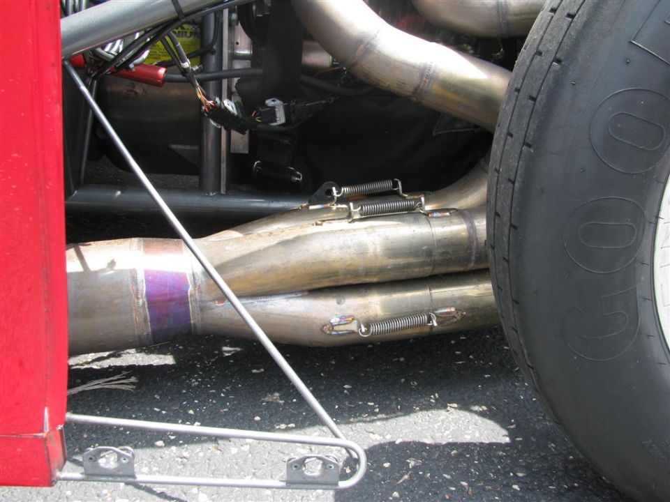 Close-up of a car's exhaust pipes and a Goodyear tire. Red body panel visible on the left