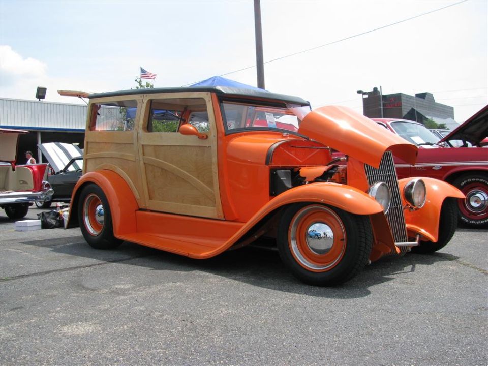Orange woody hot rod with hood open, parked next to a red car