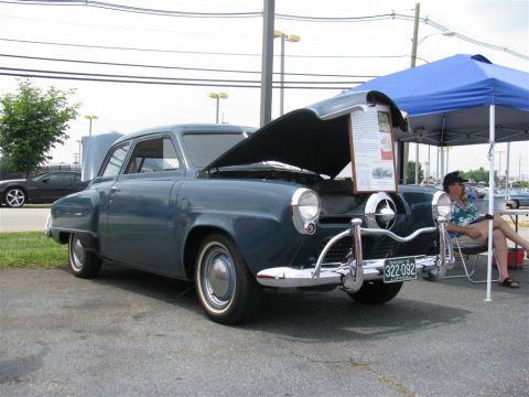 2003 Mercury Marauder - A blue 1947 Studebaker Champion sedan is displayed with its hood open at a car show, with a person sitting nearby under a tent.