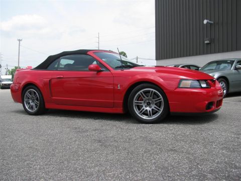 2003 Mercury Marauder - A red convertible Mustang is parked in front of a building with other vehicles nearby.