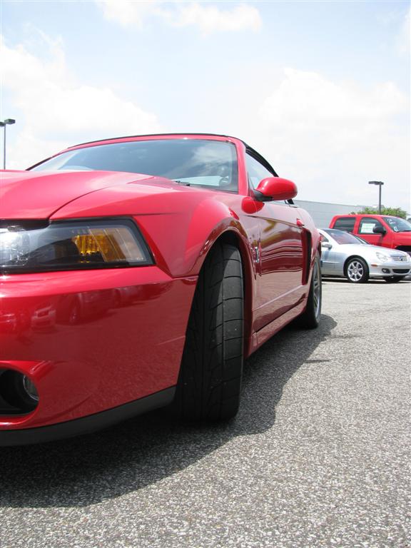 Red convertible sports car, front quarter view, with black soft top up. Visible tire and fender