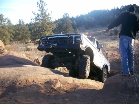 1978 Ford Bronco - A person directs an off-road SUV as it navigates a challenging rocky trail.