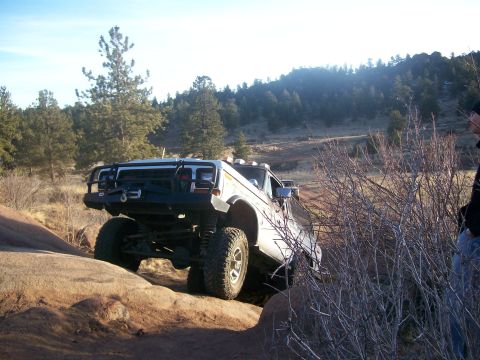 1978 Ford Bronco - A modified white off-road vehicle navigates a rocky trail with a person standing nearby.