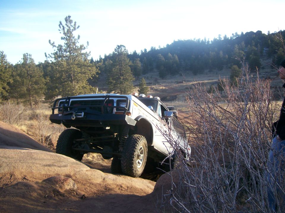White off-road vehicle with aftermarket bumper and winch climbing rocks