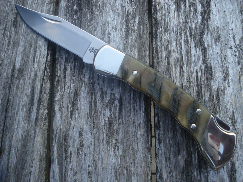 Buck folding knife with horn handle and polished bolsters on wooden surface