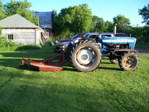 2000 Chevrolet Tahoe - Tractor with mower attachment in a grassy yard, with a building and another vehicle in the background.