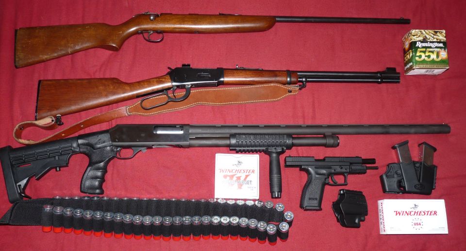 Three firearms, ammunition boxes, and shell belts on a red surface