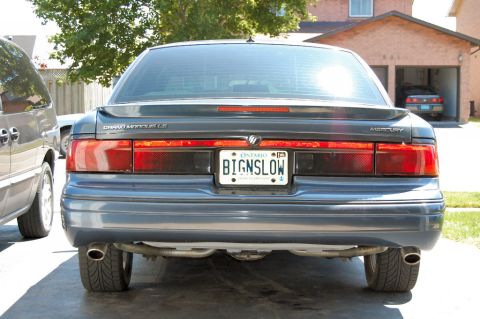 1985 Mercury Grand Marquis - Rear view of a Mercury Grand Marquis, showing its taillights and license plate. A second vehicle is parked nearby.