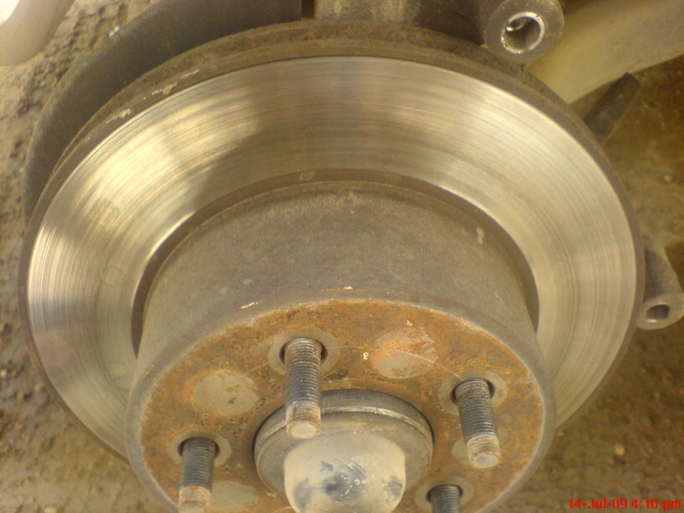 Close-up of a rusty brake rotor and hub assembly with visible lug studs