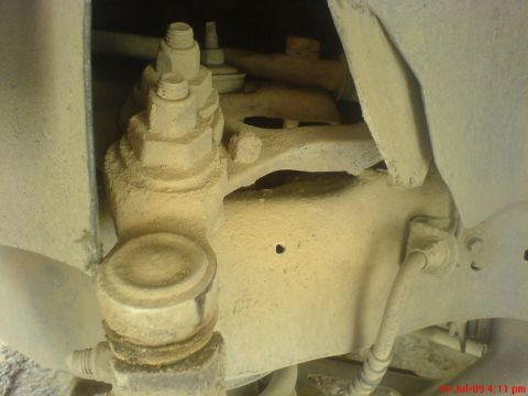 1992 Ford Crown Victoria - Underside view of a front suspension corner buried in pale dust, showing the cast steering knuckle, upper ball joint with its castellated n…
