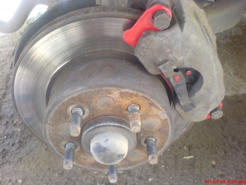 1992 Ford Crown Victoria - Front brake photographed with the wheel off, showing a vented rotor with a heavy outer wear lip and a rust-coated five-lug hub with bare st…