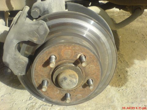 1992 Ford Crown Victoria - Close-up of a front brake with the wheel removed, showing a vented rotor with a pronounced wear lip on its outer edge and a rusty five-lug…