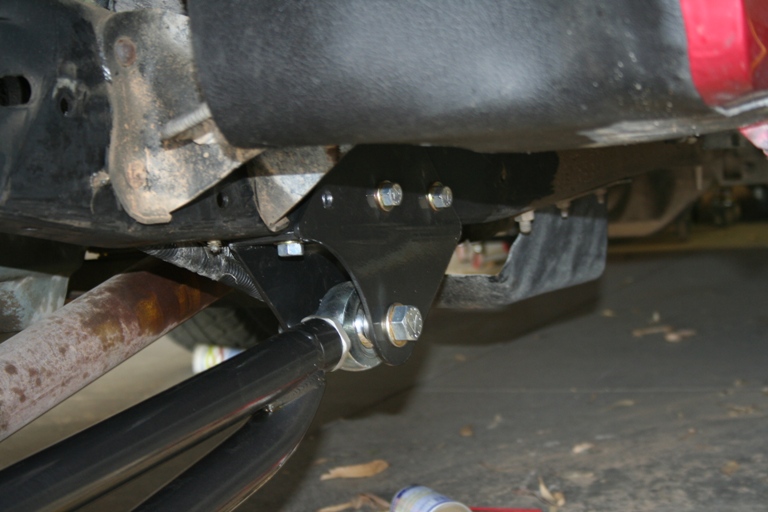 Close-up of an aftermarket suspension component bolted to a vehicle's frame, with part of the exhaust visible