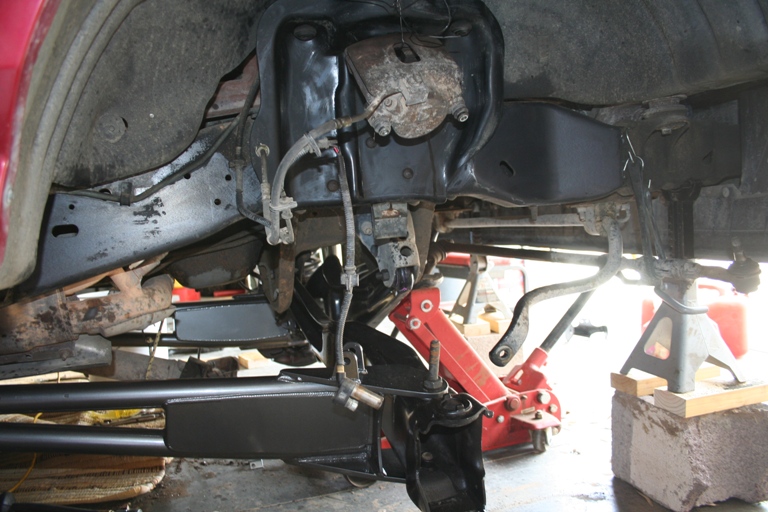 Underside view of a vehicle's front suspension with parts removed, supported by jack stands