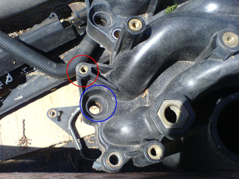 Black plastic intake manifold close-up with red and blue circles highlighting a threaded boss and a port