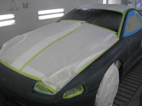 1987 Suzuki Samurai - A car is prepared for painting in a spray booth, with the hood and front fender taped off. A Mitsubishi logo is visible on the fender.