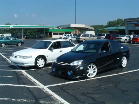 1993 Ford Taurus - A black sedan with custom white rims is parked in a lot next to a white sedan.