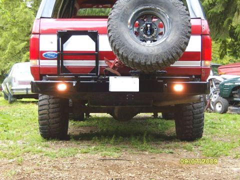 1989 Ford Bronco - The rear of a red Ford Bronco shows a spare tire mounted on the back, along with a custom bumper and tow hitch.