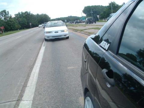 1993 Ford Taurus - A black car is seen from the side on a highway, with another white car ahead.