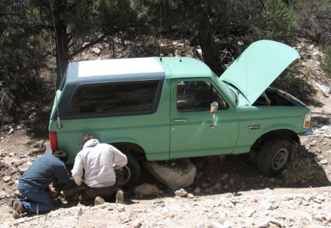 1996 Ford Bronco - Two people attempt to free a green Ford Bronco that is stuck on large rocks off-road.