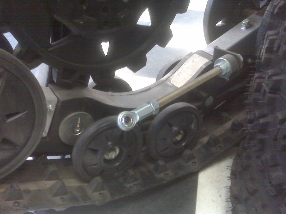 Snow track suspension with black bogie wheels and adjustable threaded link with rod end.