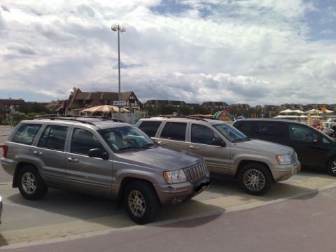 1991 Ford Crown Victoria - Two Jeep Grand Cherokees are parked in a lot near buildings under a cloudy sky.