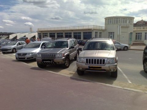 1991 Ford Crown Victoria - Two Jeep Grand Cherokees are parked in a lot with a building in the background.