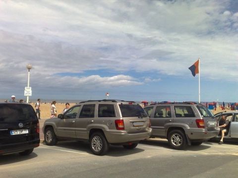 1991 Ford Crown Victoria - Two Jeep Grand Cherokees are parked in a lot with a beach and ocean in the background under a cloudy sky.