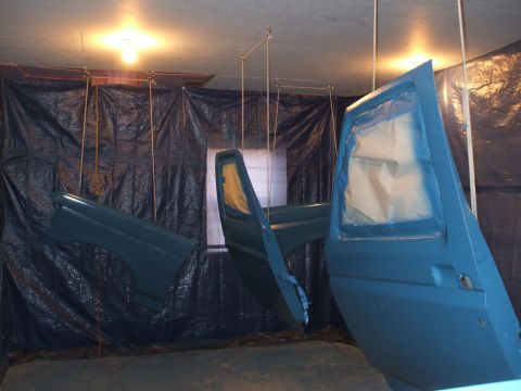 1990 Ford Bronco - Car doors and a fender are suspended and being painted inside a makeshift booth.
