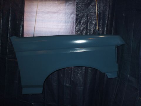 1990 Ford Bronco - A teal car fender is shown hanging against a dark tarp, likely during a painting process.