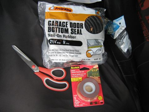 2000 Mercury Grand Marquis - A Frost King garage door bottom seal kit, along with scissors and Scotch mounting tape, are laid out on a dark surface.