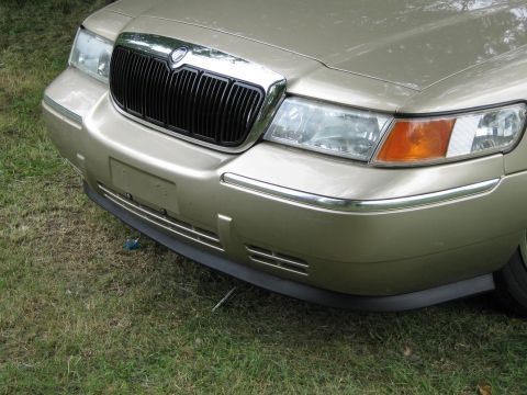 2000 Mercury Grand Marquis - The front grille and headlights of a gold sedan are visible, parked on grass.