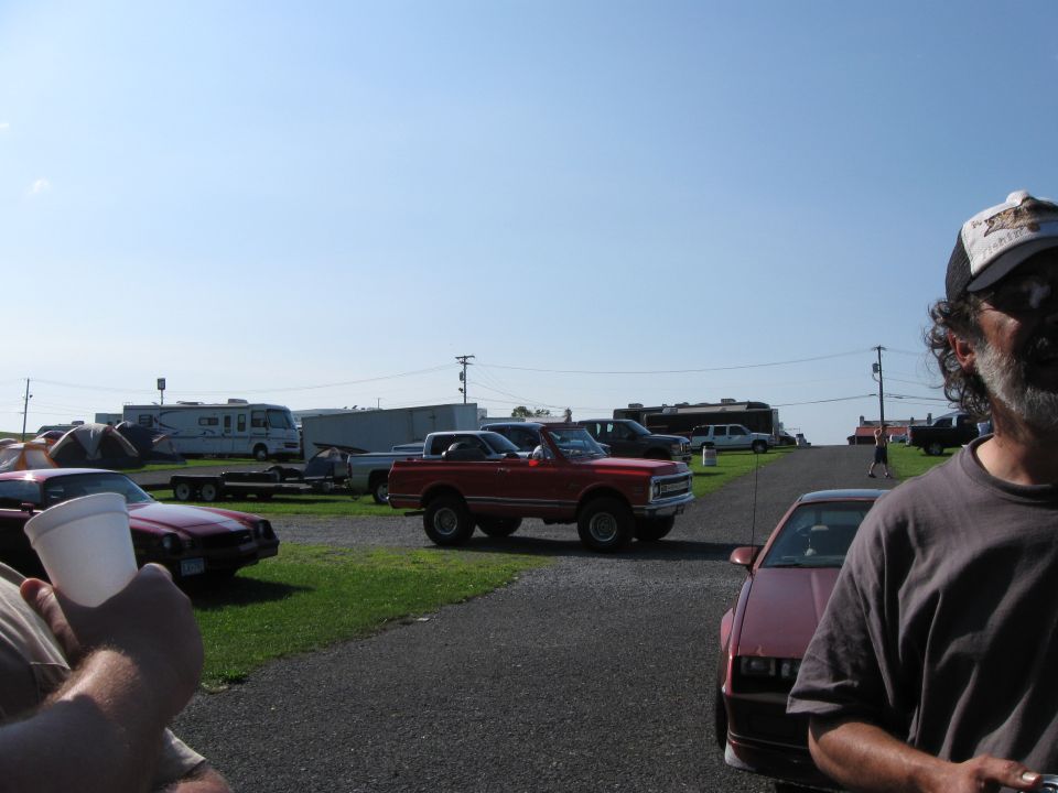 Red convertible SUV parked on gravel lot with other vehicles and tents in background