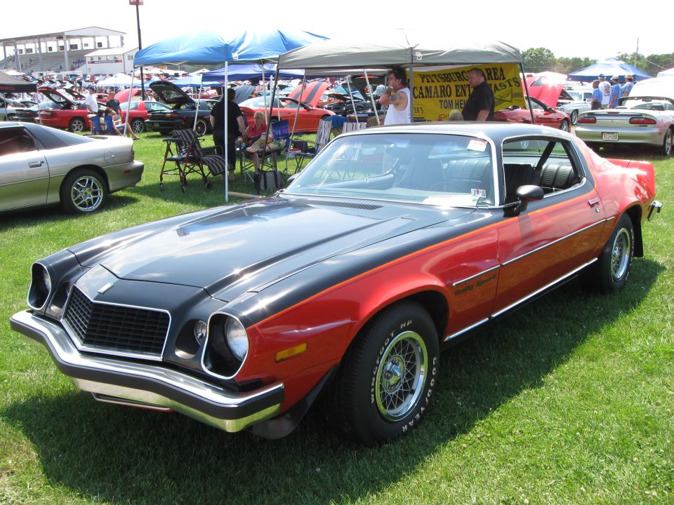 Two-tone black and red 1974 Chevrolet Camaro parked on grass at a car show