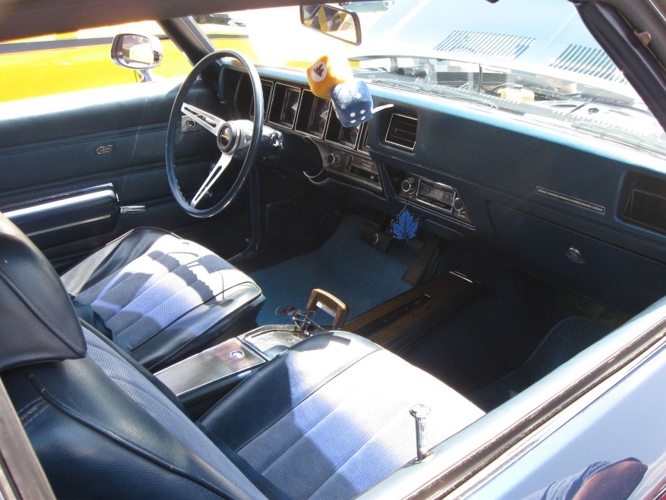 Interior view of a classic car with blue seats and dashboard, showing steering wheel and gear shifter