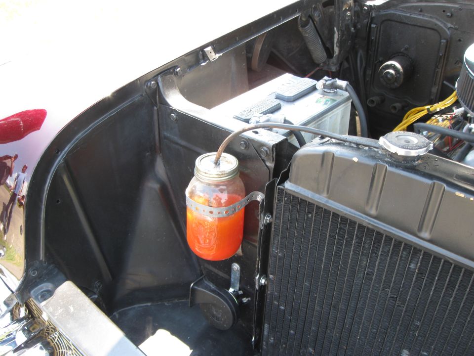 Engine bay with a mason jar holding orange fluid, mounted next to the radiator and battery