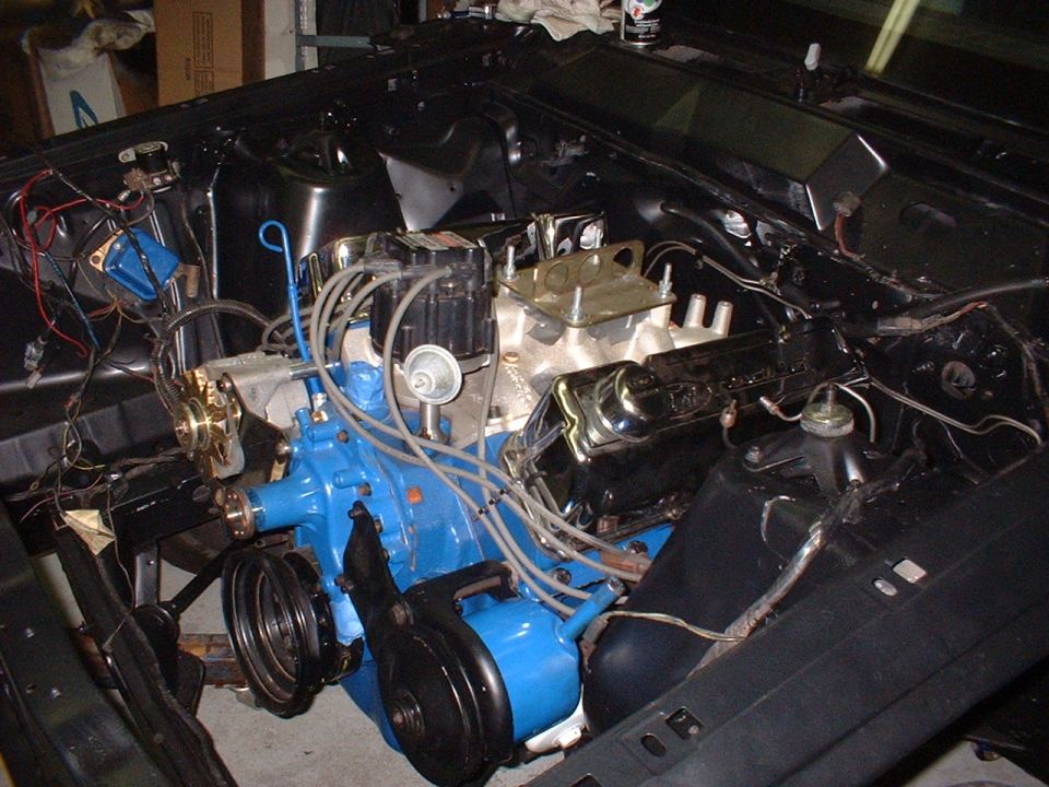 Blue V8 engine installed in black engine bay of a car under restoration in a garage
