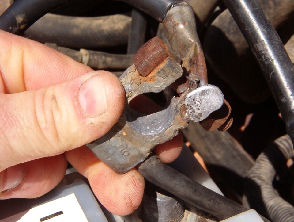 Hand holding a rusty metal bracket with cast number among engine bay hoses